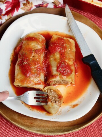 two vegan cabbage rolls on a white plate with fork and knife