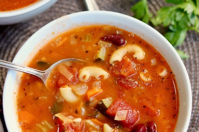 vegan minestrone soup in a white bowl with a spoon