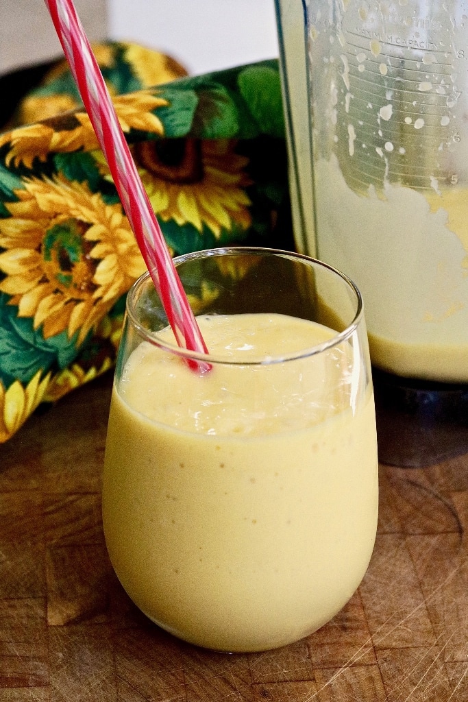 mango smoothie in a glass beside a blender