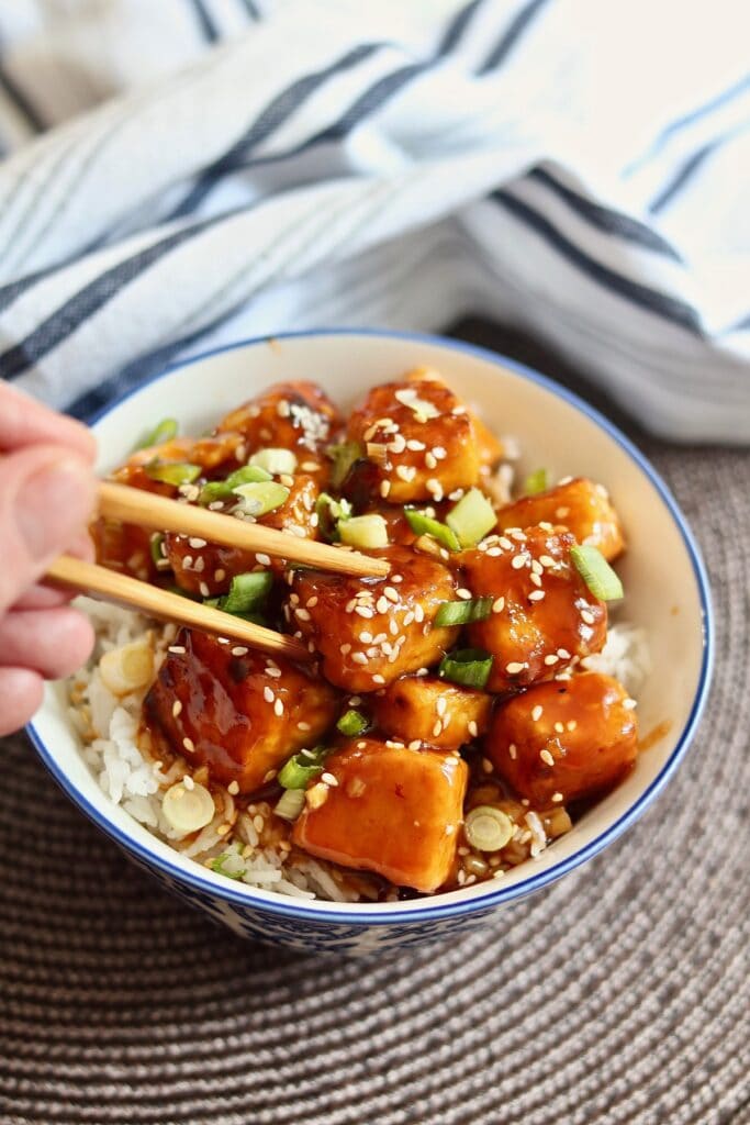 general tso tofu ready to serve in a bowl with chopsticks