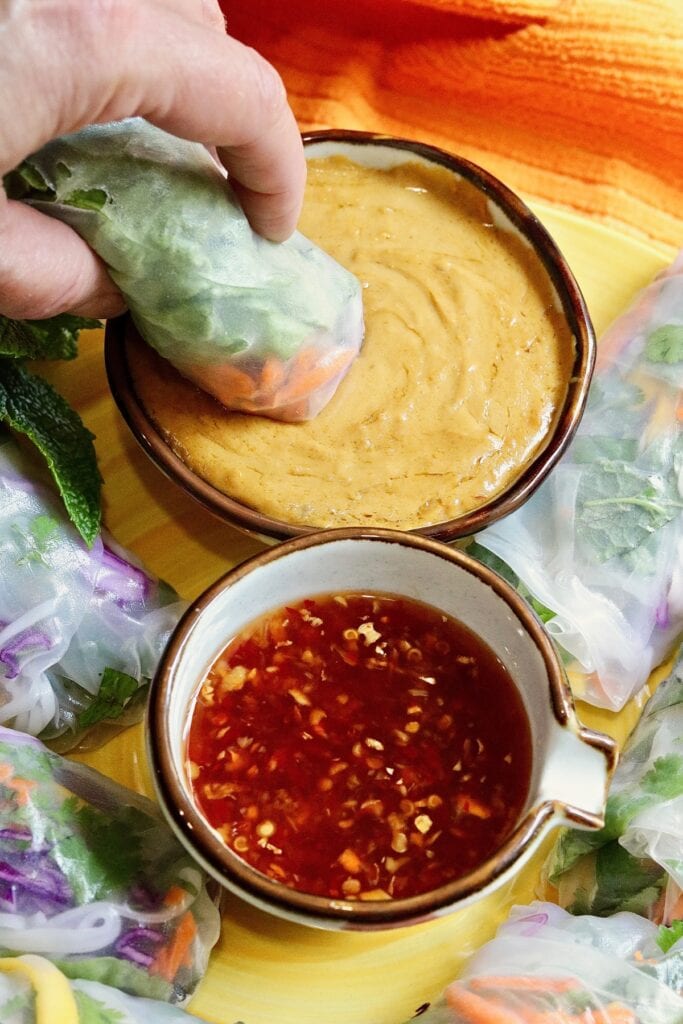 fresh spring roll being dipped in peanut sauce 