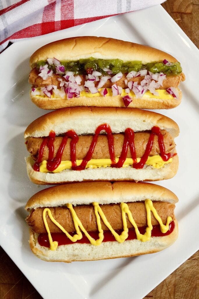 three vegan hot dogs in buns on a plater with toppings