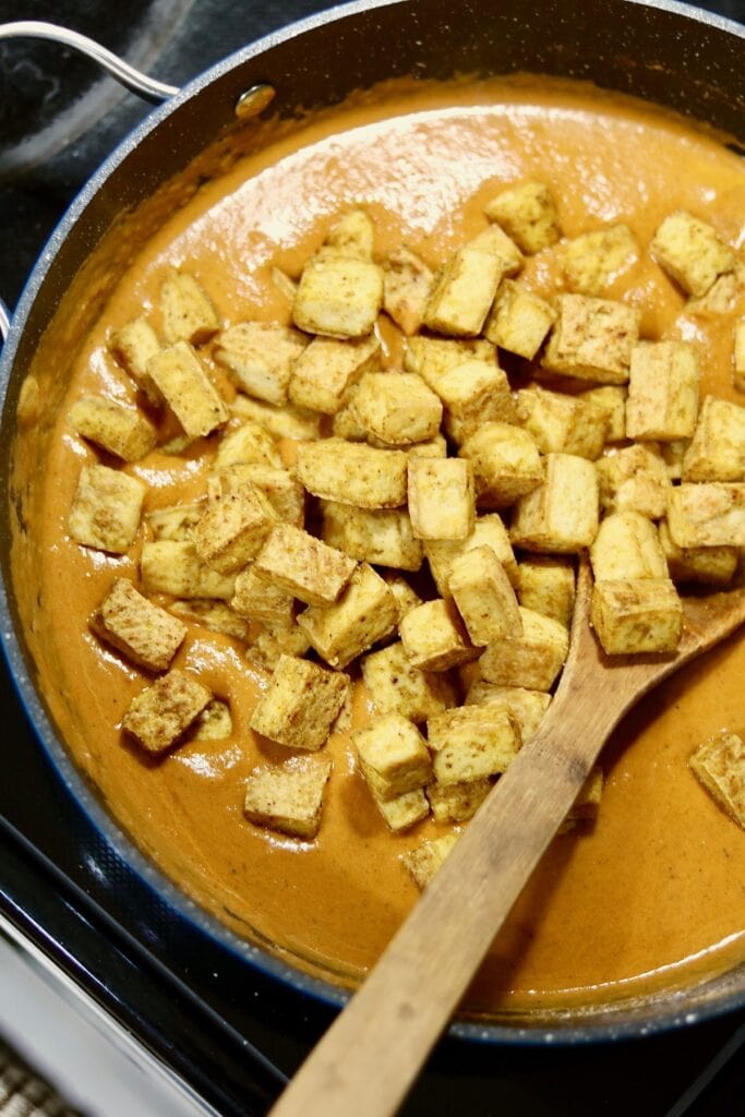 overhead view tikka masala sauce ingredients in a large pan simmering and topped with tofu