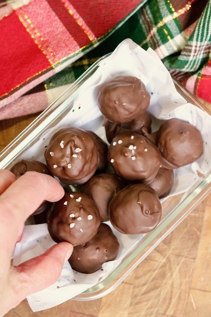 chocolate peanut butter ball being picked up out of a holiday container 