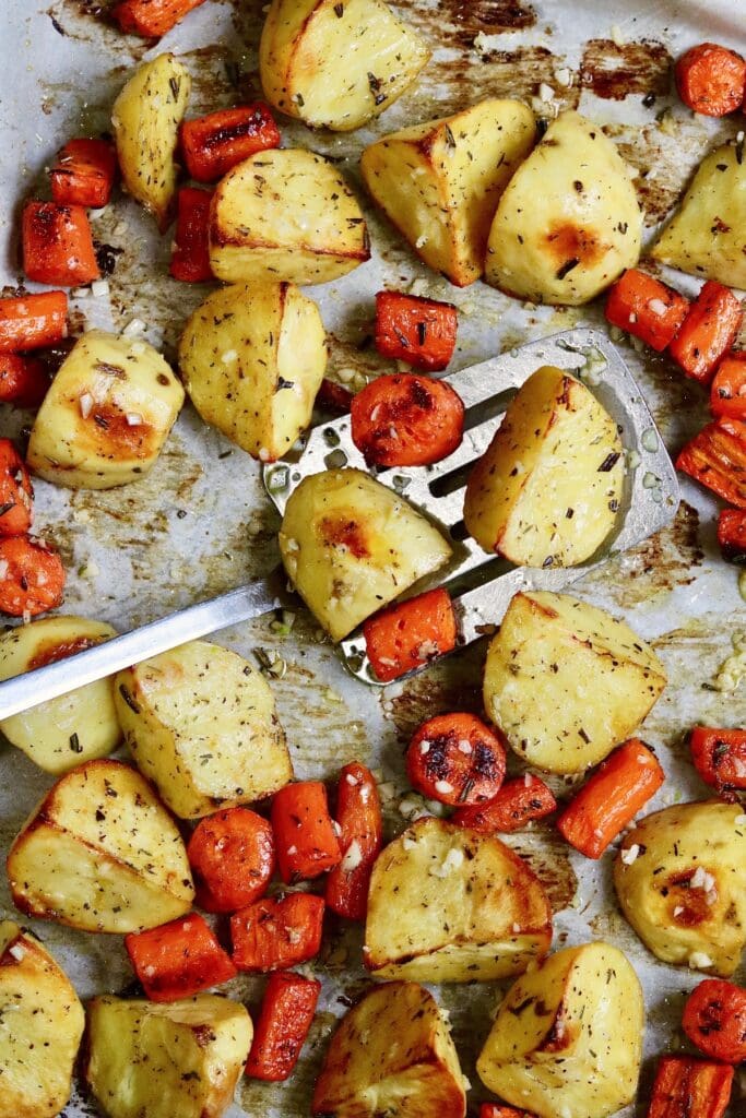 roasted potatoes and carrots with spatula on a baking sheet ready to serve