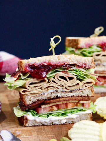 vegan cranberry and turkey club sandwich sliced in half on a cutting board