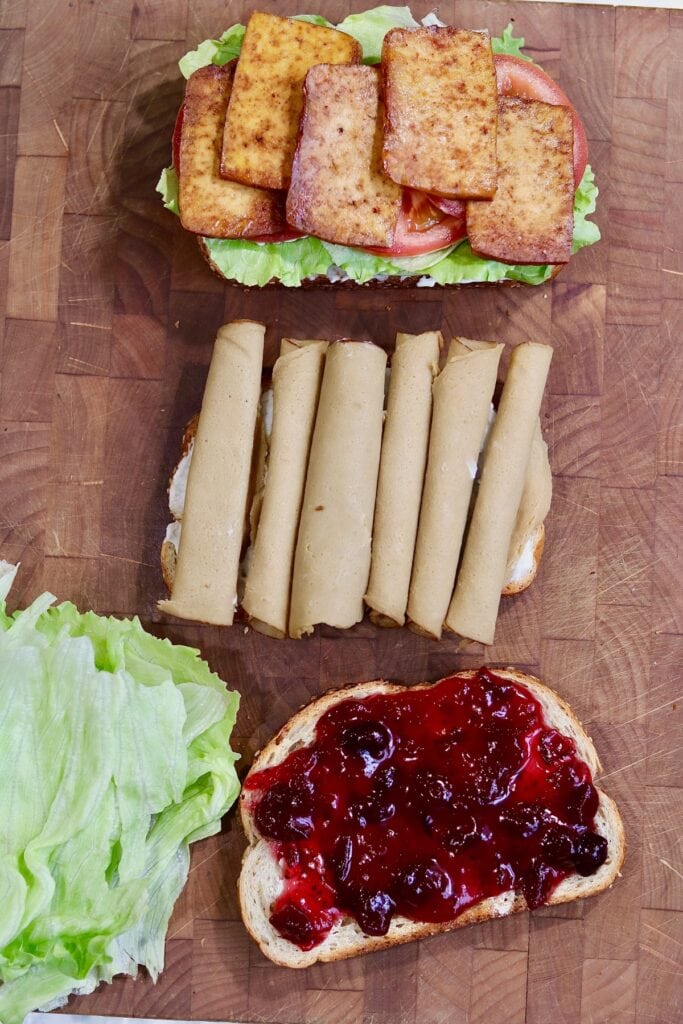 vegan cranberry and turkey club sandwich being made on a cutting board