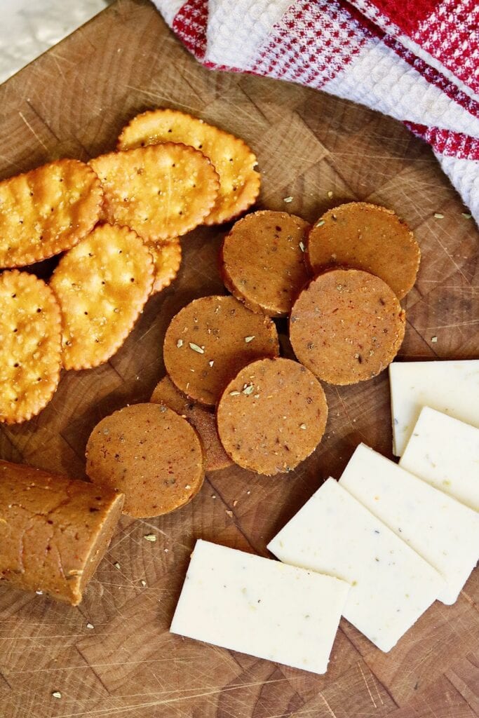 vegan pepperoni sliced on cutting board with cheese and crackers ready for pizza or charcuterie platter