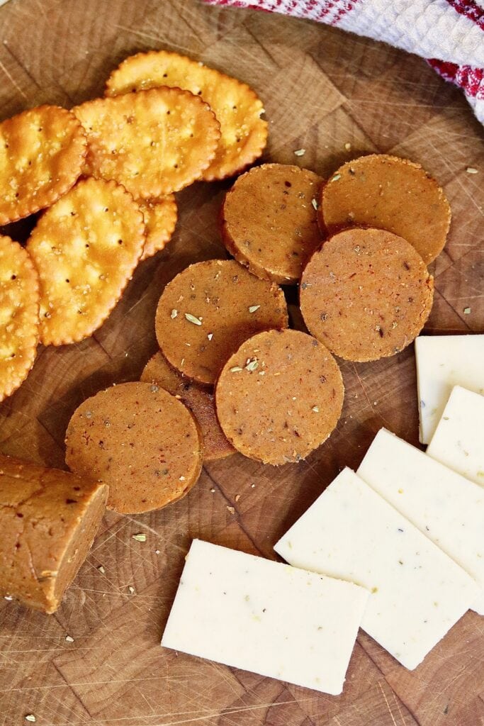 vegan pepperoni sliced on a cutting board with cheese and crackers