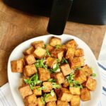 air fried tofu on a plate beside an air fryer