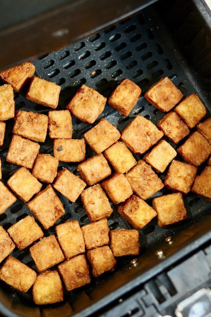 overhead view of crispy cooked tofu cubes in air fryer basket