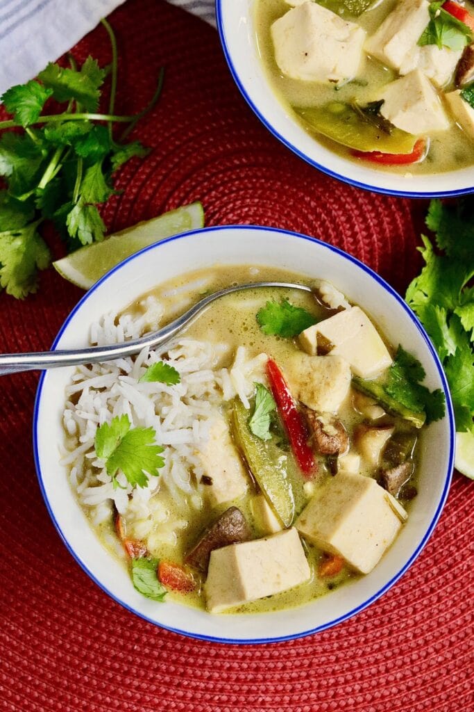 a bowl of thai green curry with tofu and vegetables in a bowl with rice