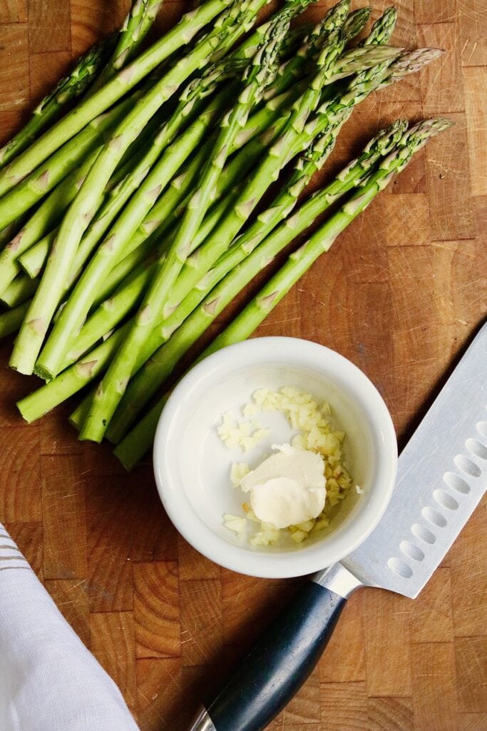asparagus trimmed on a cutting board beside a bowl of garlic butter
