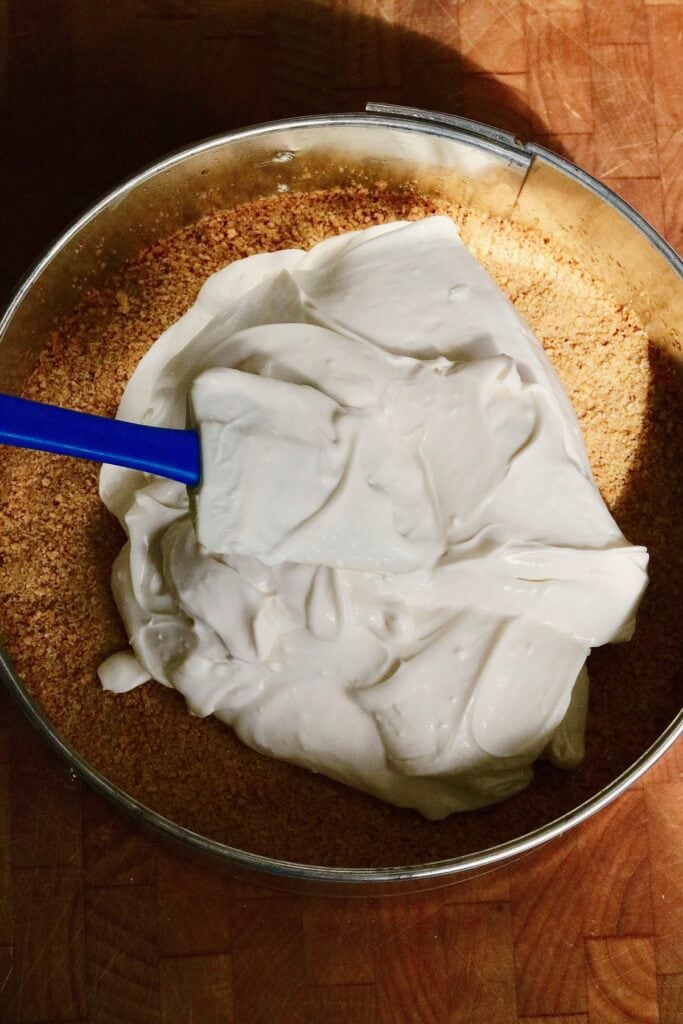 cheesecake filling ingredients being poured on graham wafer crust