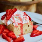 a slice of vegan strawberry shortcake cake on a plate topped with whipped cream and strawberries