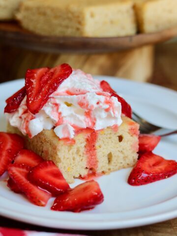 a slice of vegan strawberry shortcake cake on a plate topped with whipped cream and strawberries