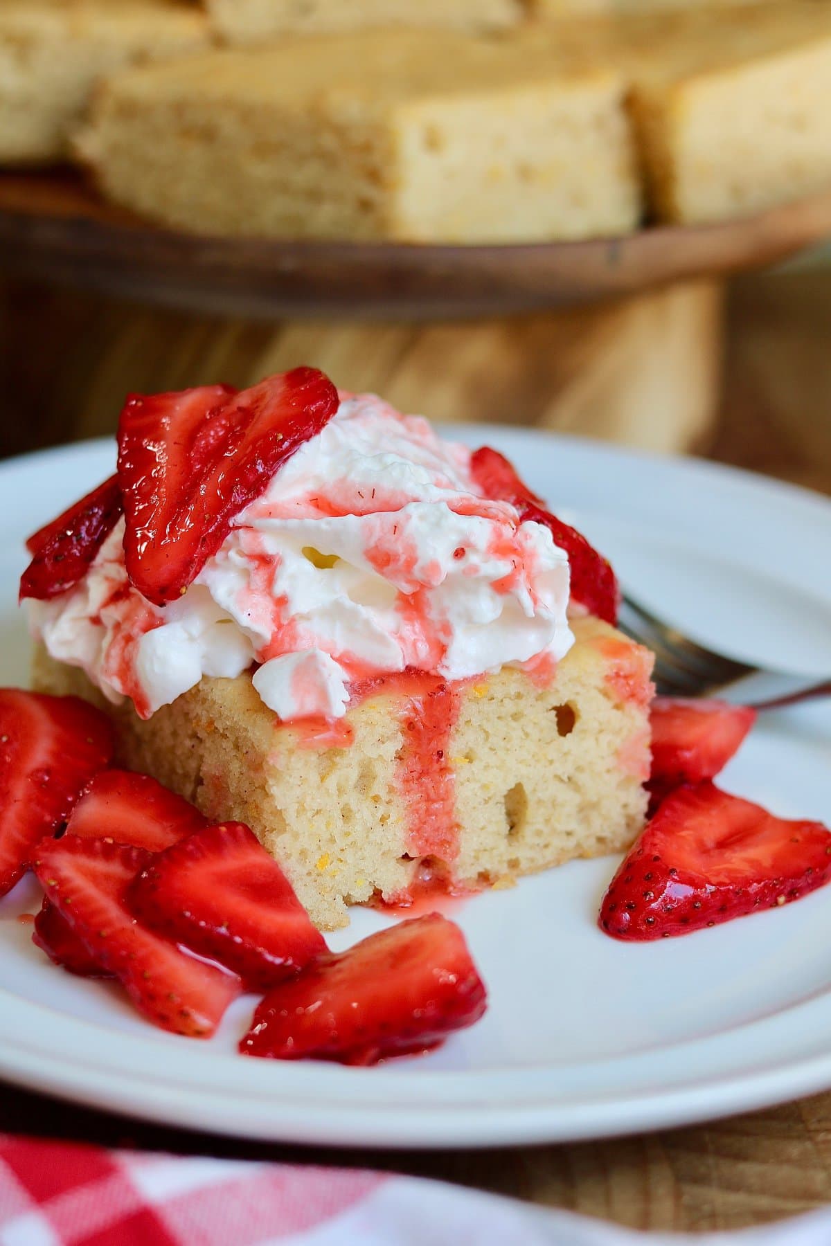 a slice of vegan strawberry shortcake cake on a plate topped with whipped cream and strawberries