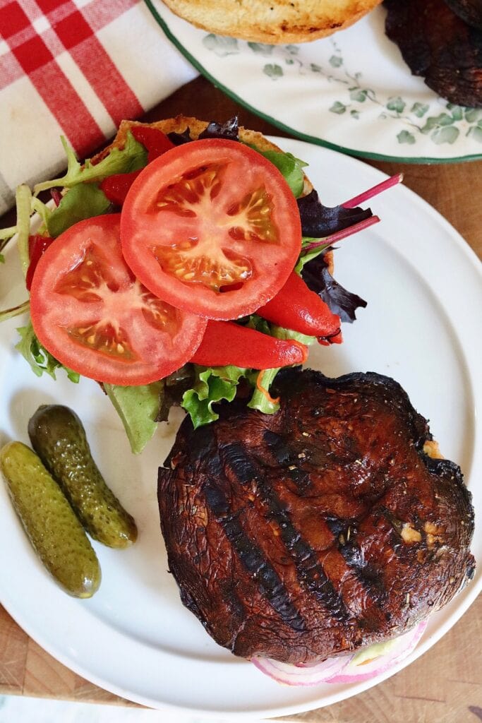 portobello mushroom burger open faced on a hamburger bun with lettuce tomatoes and side pickles 