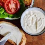 vegan tofu mayonnaise being spread on a bread slice for a sandwich with tomato and lettuce