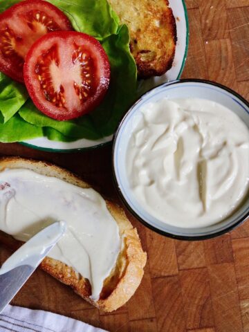 vegan tofu mayonnaise being spread on a bread slice for a sandwich with tomato and lettuce
