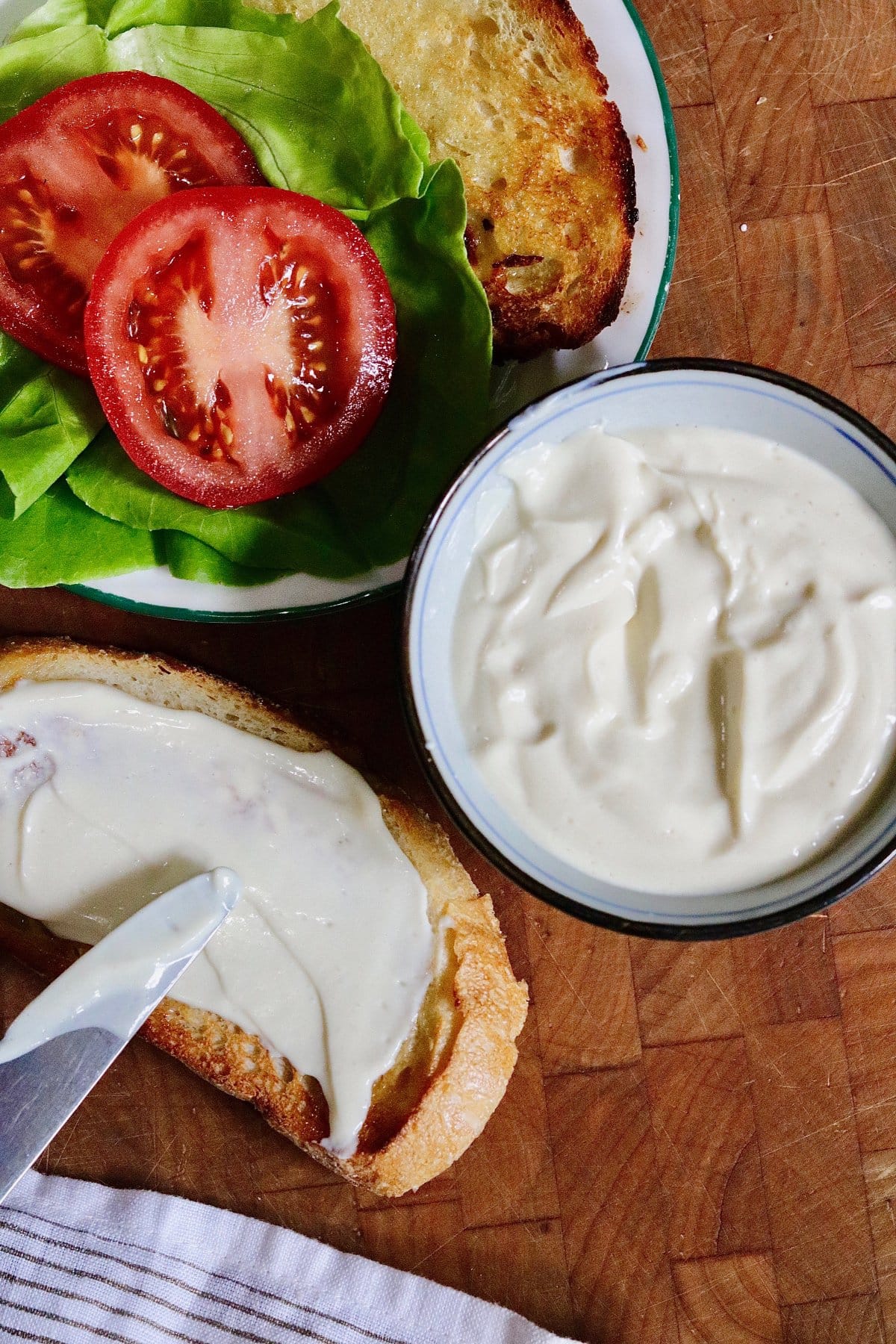 vegan tofu mayonnaise being spread on a bread slice for a sandwich  with tomato and lettuce