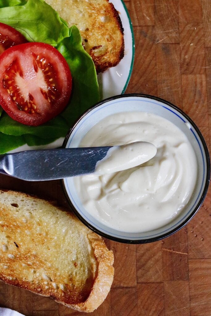 tofu mayonnaise in a bowl beside toasted bread and lettuce and sliced tomatoes