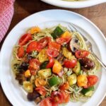 pesto pasta on a plate topped with cherry tomatoes and roasted vegetables