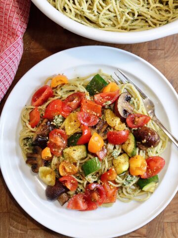 pesto pasta on a plate topped with cherry tomatoes and roasted vegetables