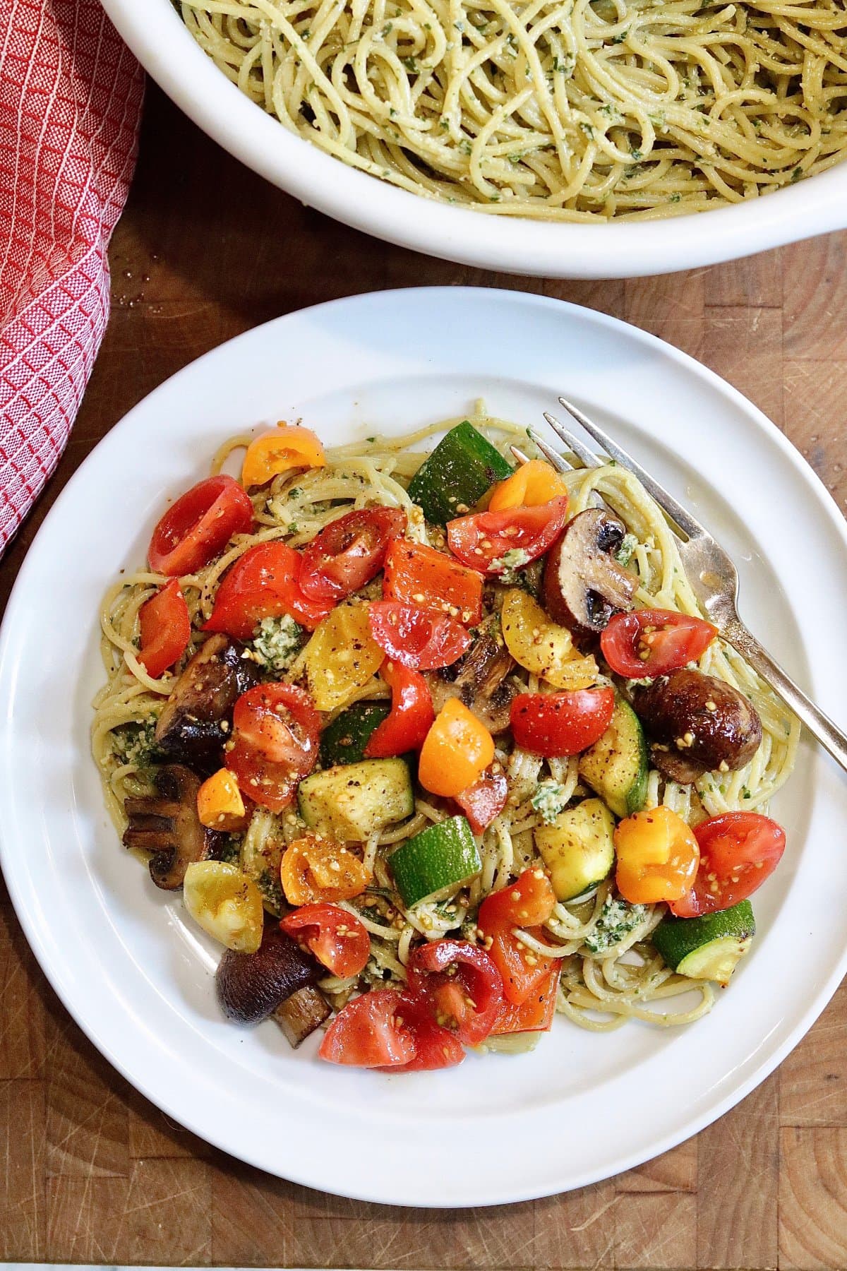pesto pasta on a plate topped with cherry tomatoes and roasted vegetables 