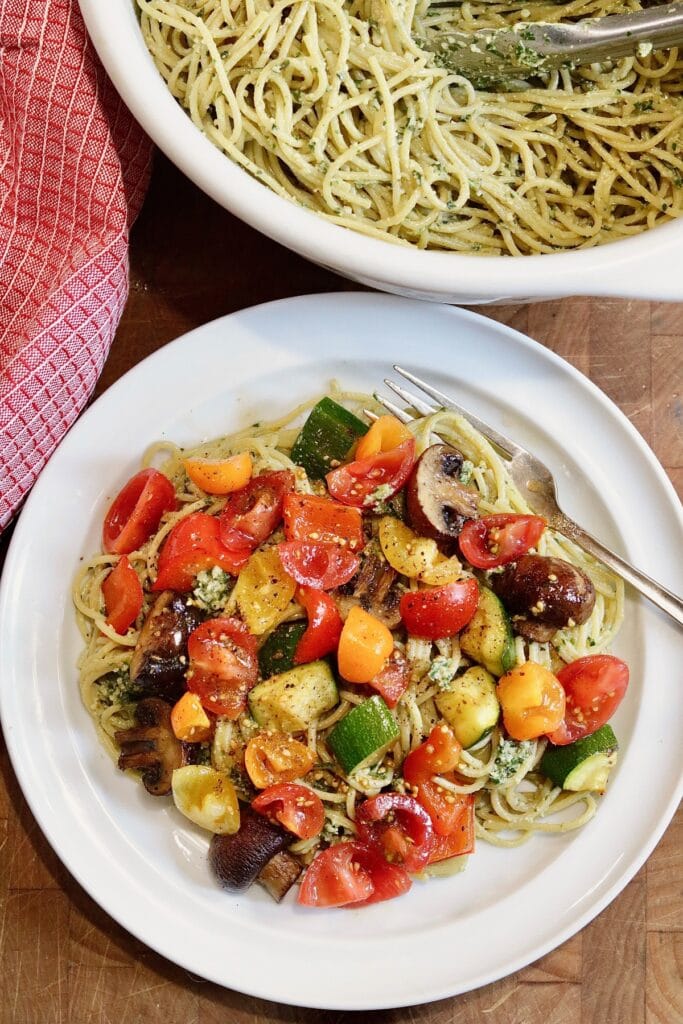cherry tomatoes and veggies topped on a plate of pesto pasta