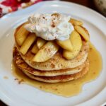 a stack of vegan apple cinnamon pancakes topped with apple compote and whipped cream