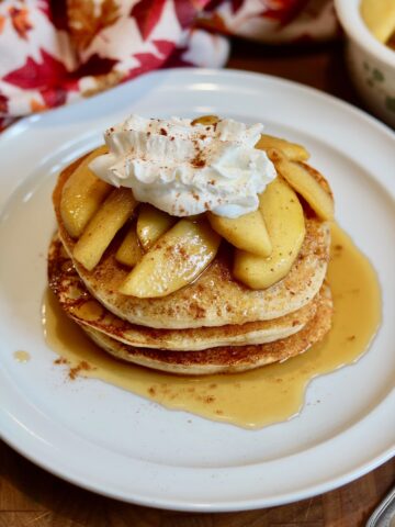 a stack of vegan apple cinnamon pancakes topped with apple compote and whipped cream