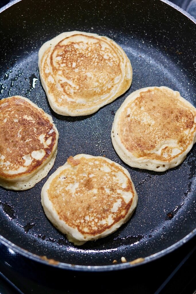 four apple cinnamon pancakes cooking in a skillet