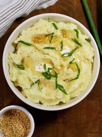 a bowl of no drain instant pot mashed potatoes topped with green onions sesame oil and vegan butter