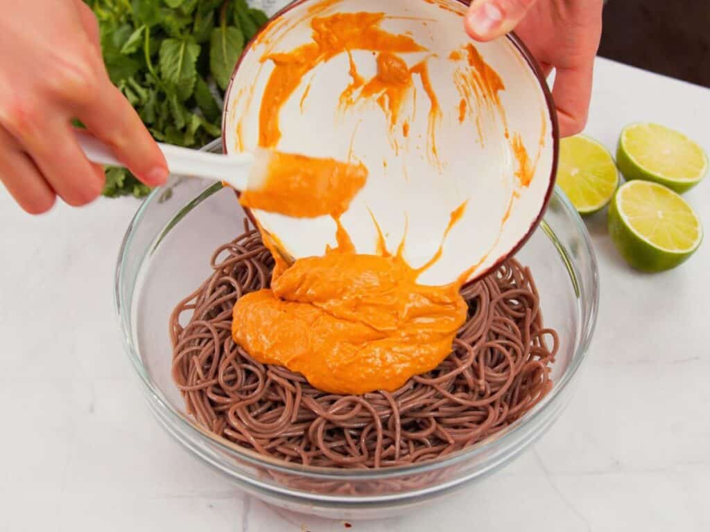 orange sauce being poured over noodles in glass bowl