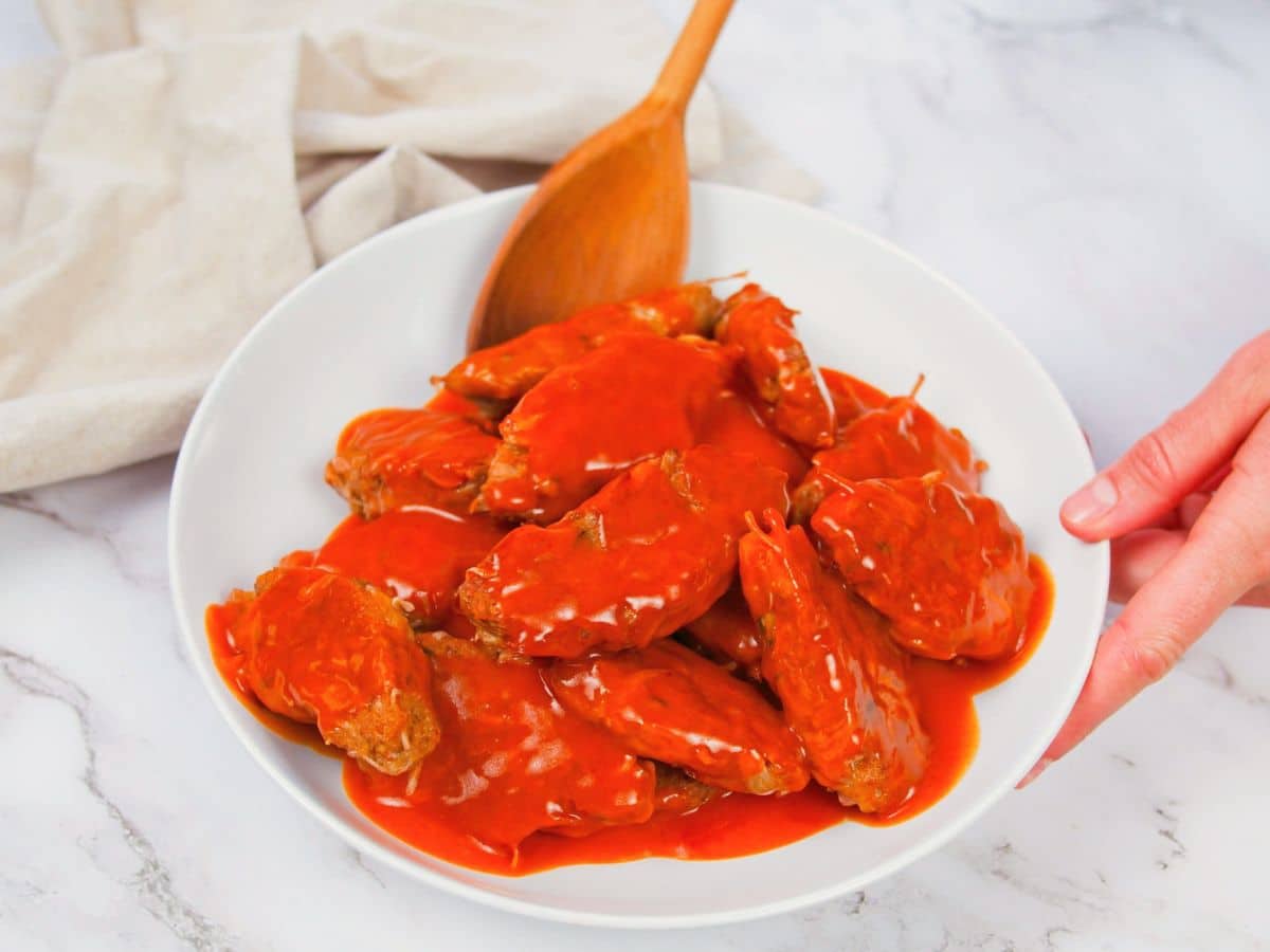 wooden spoon stirring vegan wings in white bowl with sauce