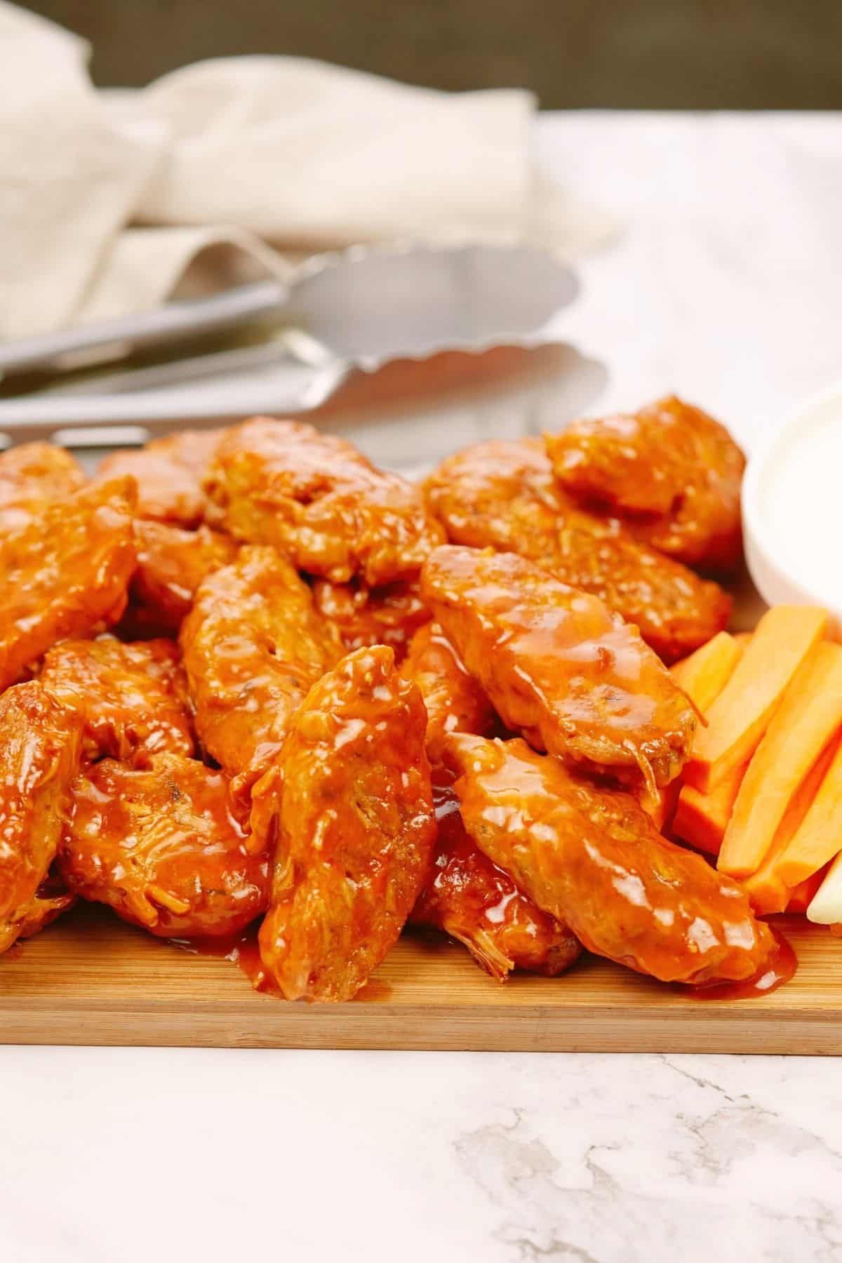 wood cutting board holding vegan wings on marble table with napkin and tongs in background