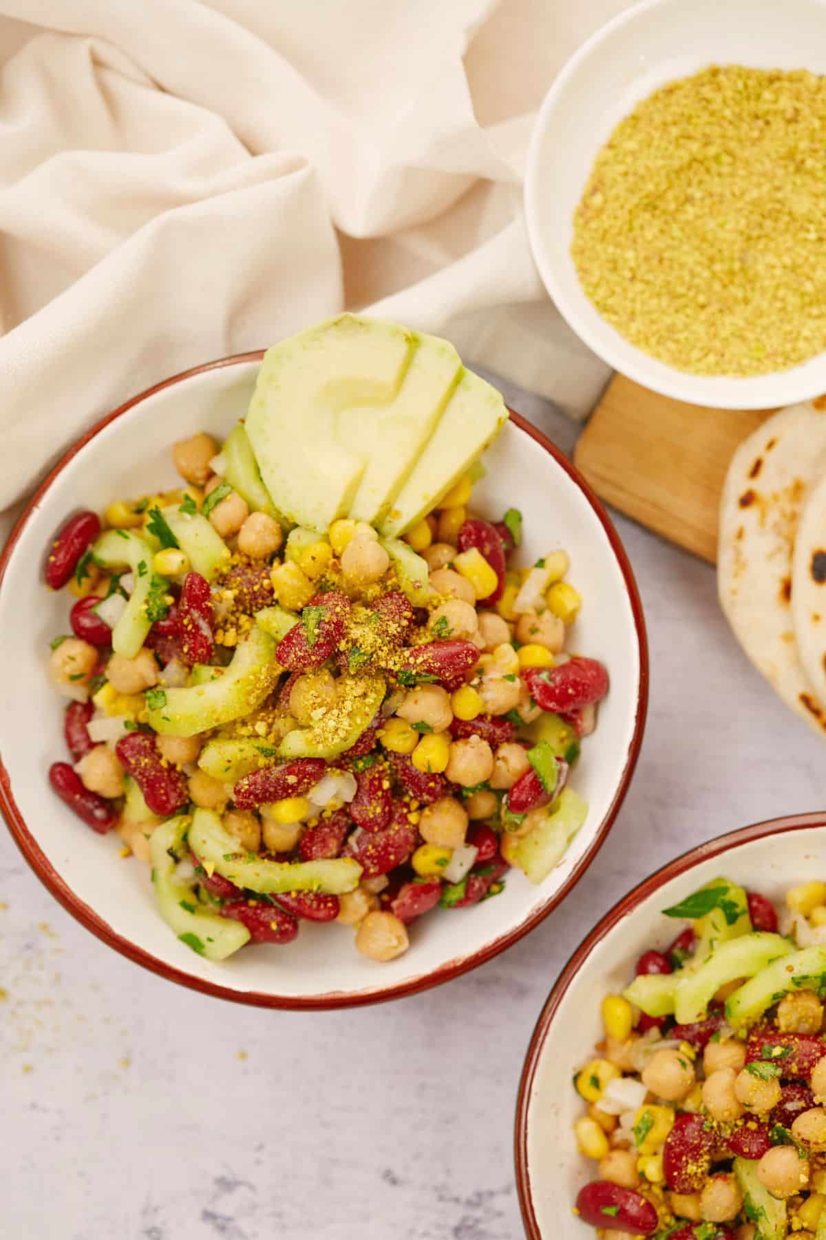 large white and red bowl of vegan kidney bean salad on table by white napkin