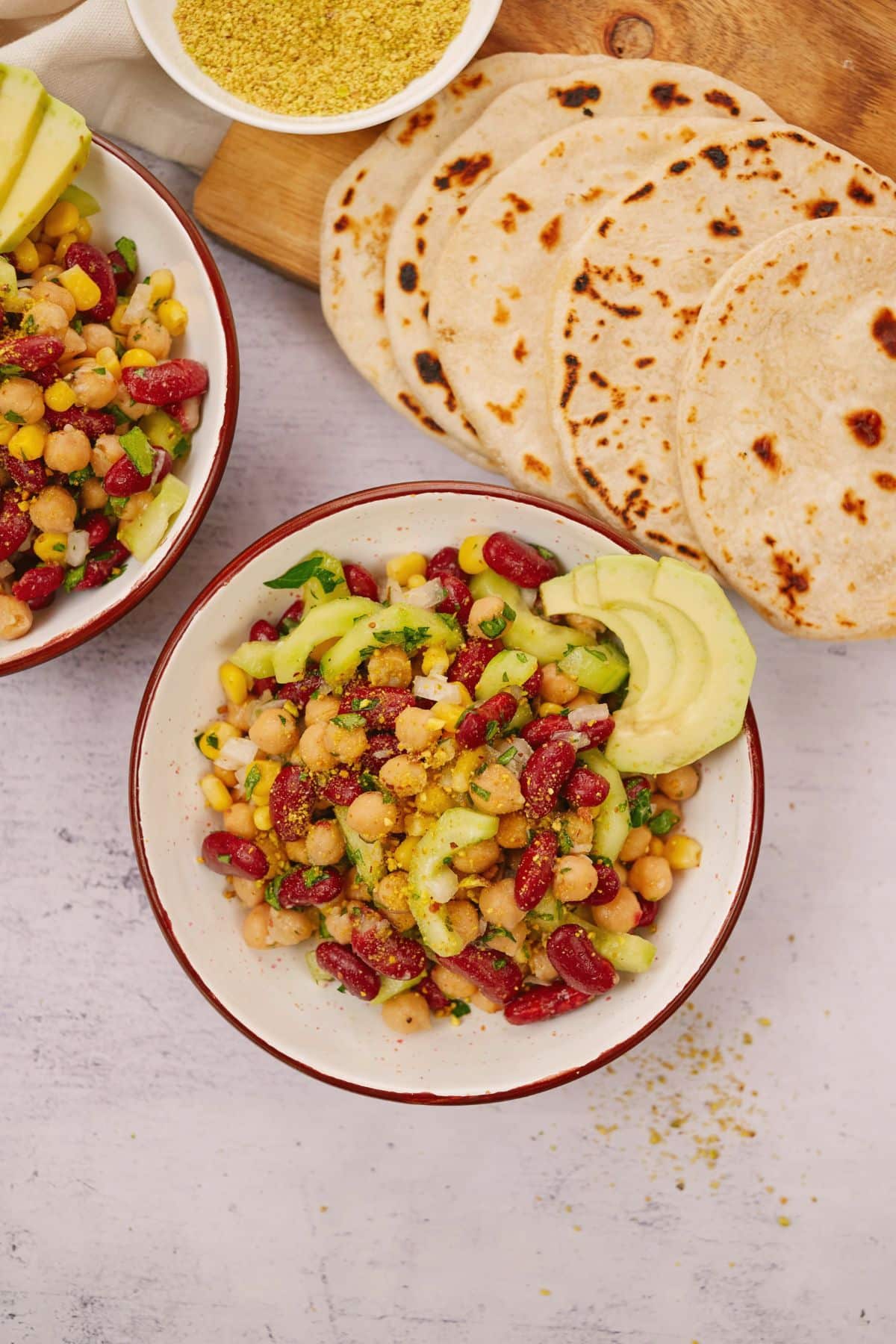 white and red bowl filled with vegan kidney  bean salad topped with sliced avocacdo