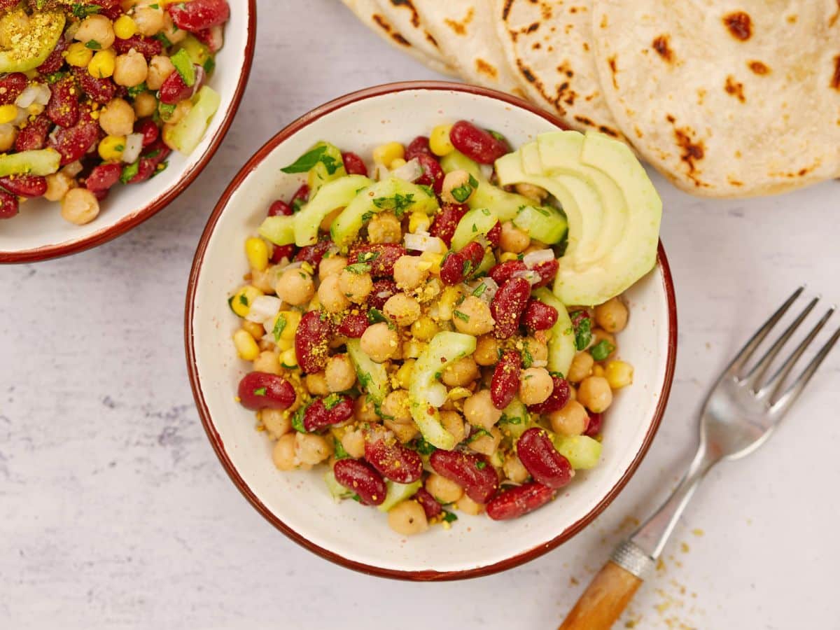 bowl of bean salad on marble table with tortillas in background