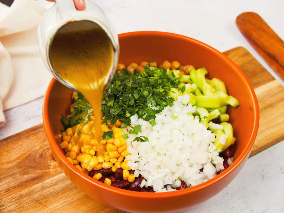 salad dressing being poured over vegetables in orange bowl