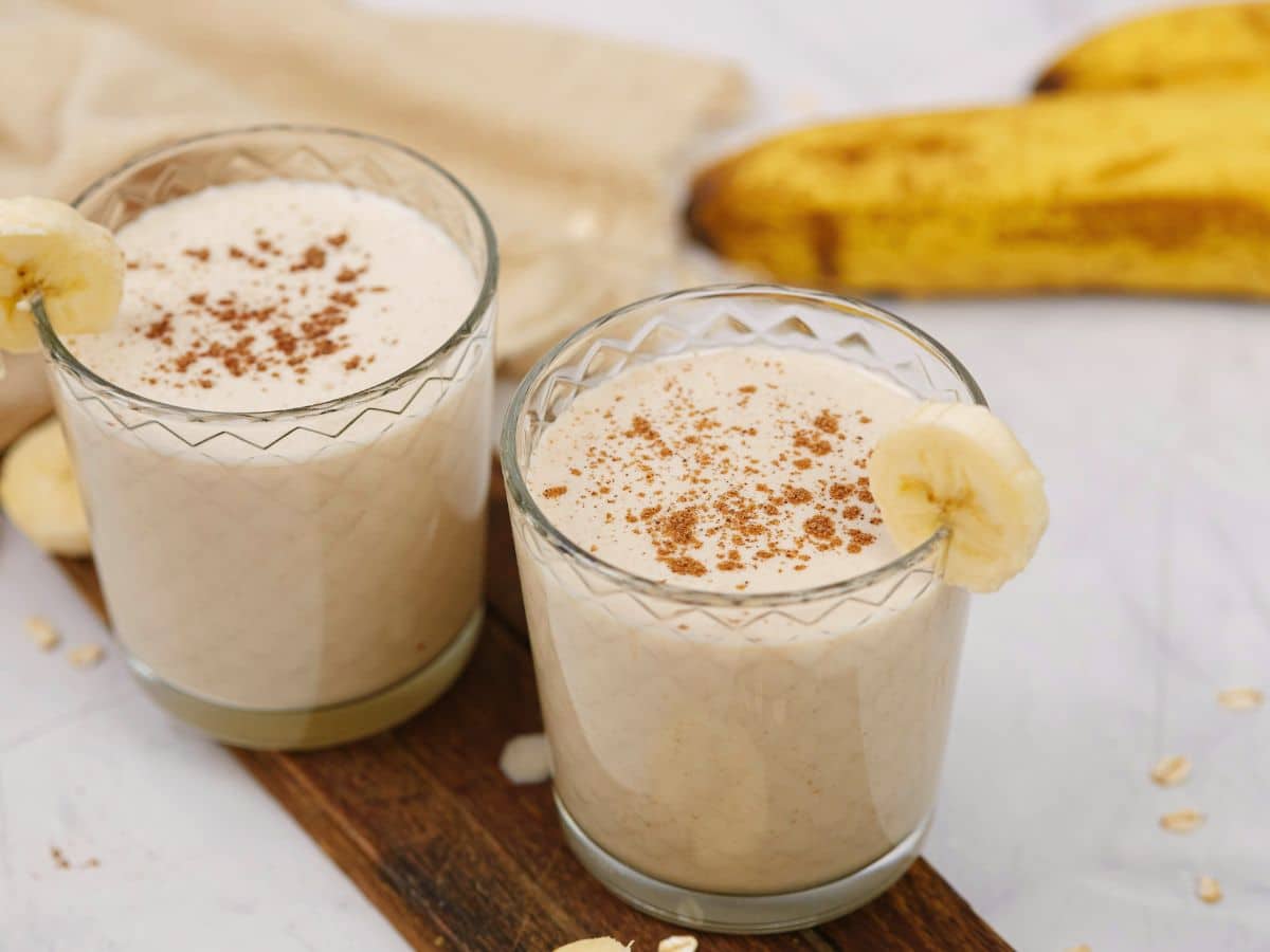 peanut butter vegan oat smoothie in two glasses with sliced bananas on rim