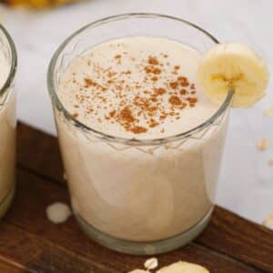 short glass filled with oat smoothie sitting on dark wood board