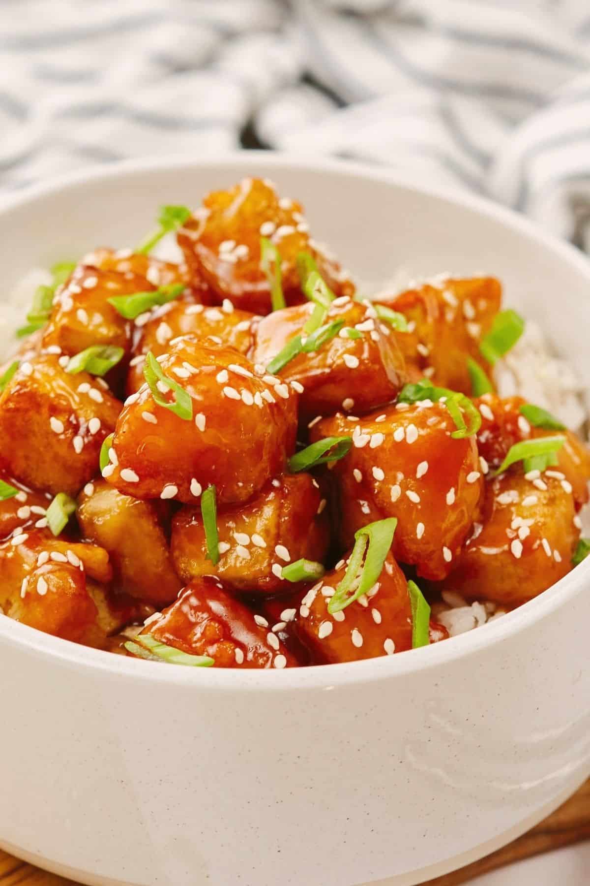 crispy fried tofu in sauce on top of rice in white bowl