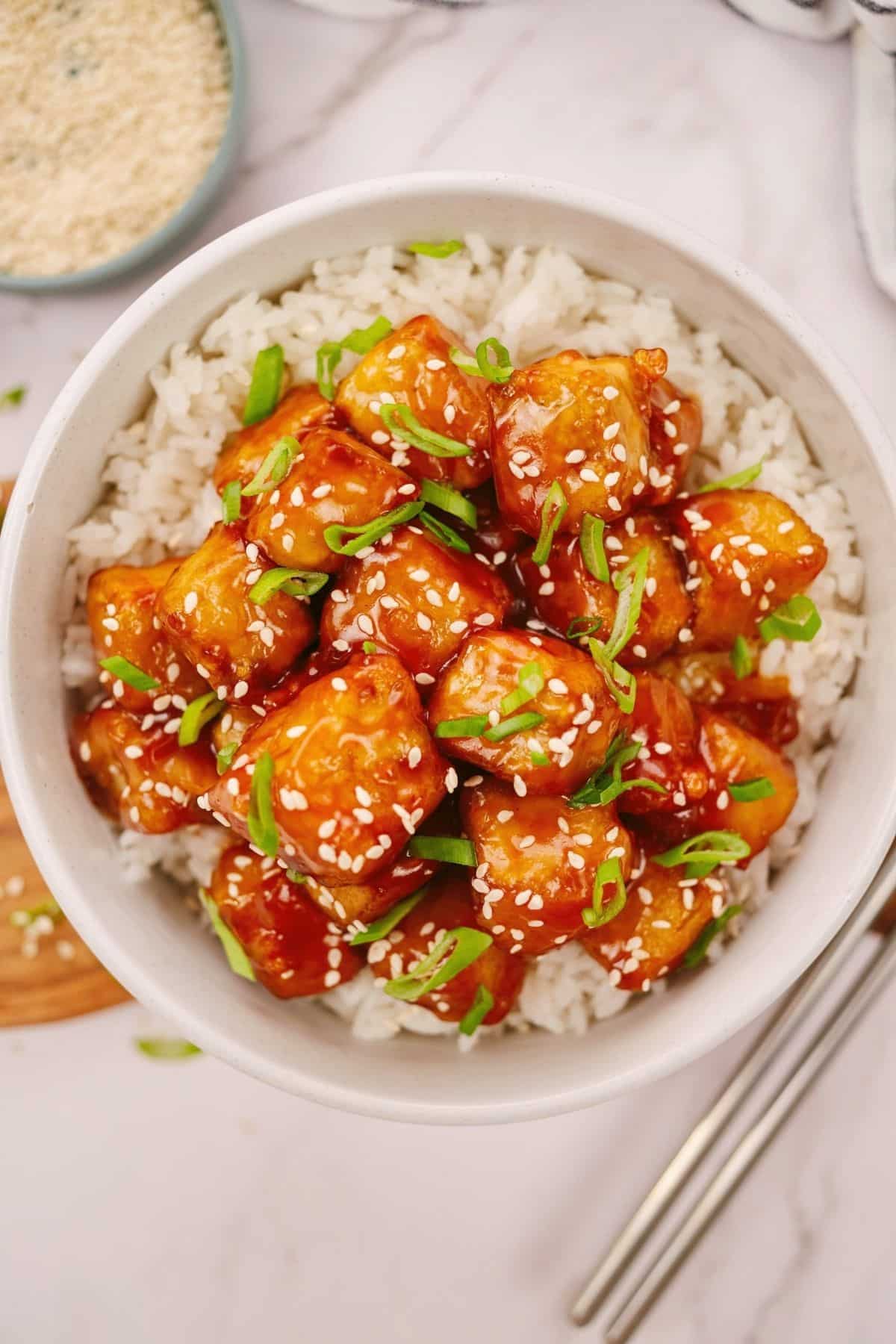 white bowl of rice topped by sweet and sour tofu