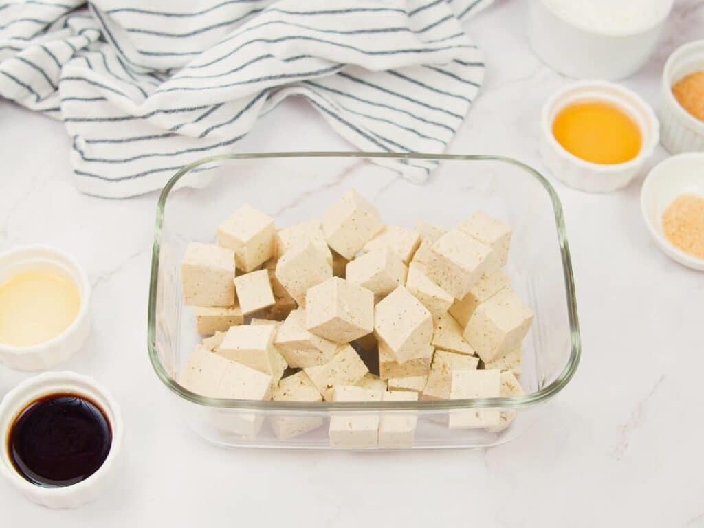 cubed tofu in glass bowl on white table by striped towel
