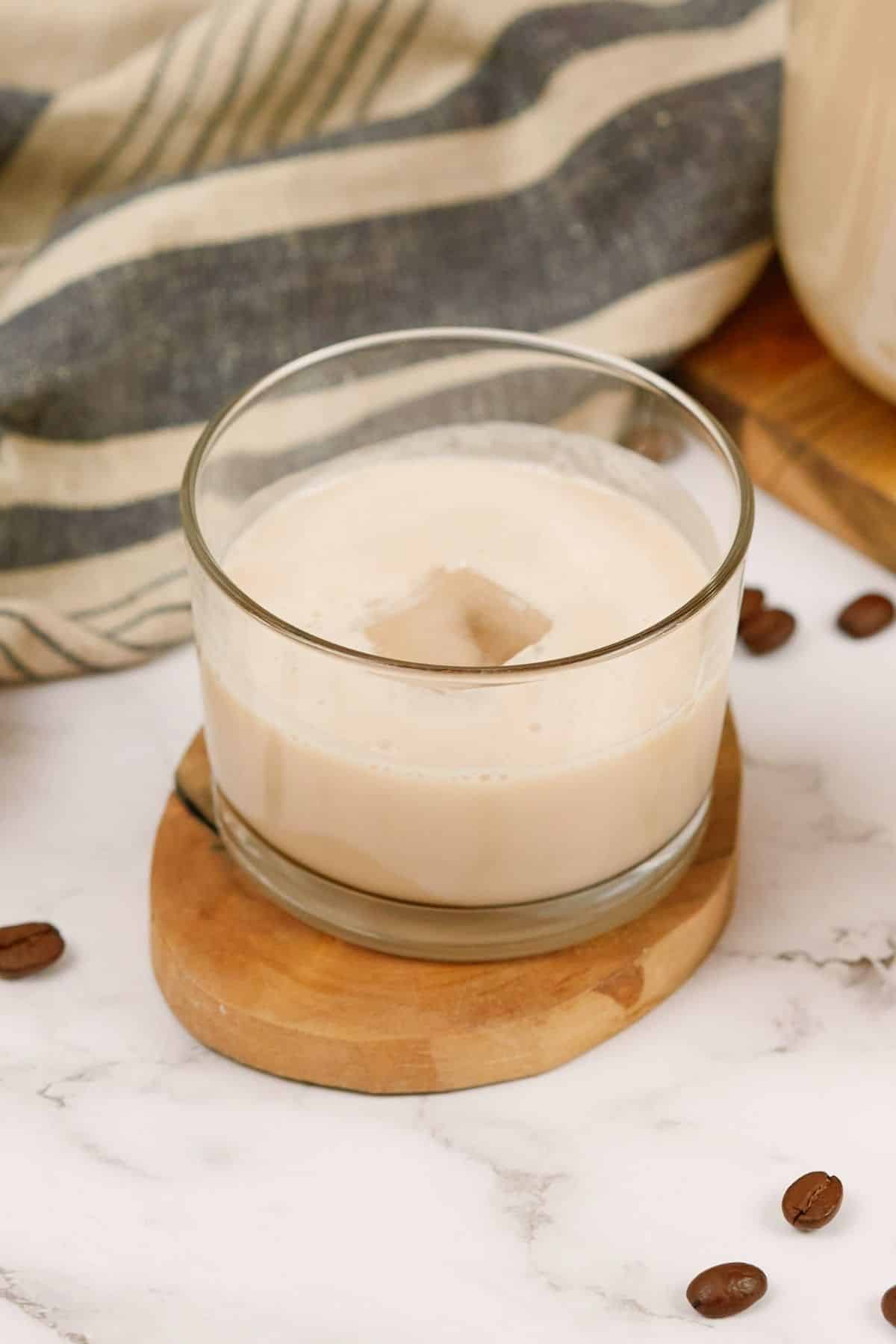 single glass of vegan Bailey's cocktail sitting on an oval wood slice