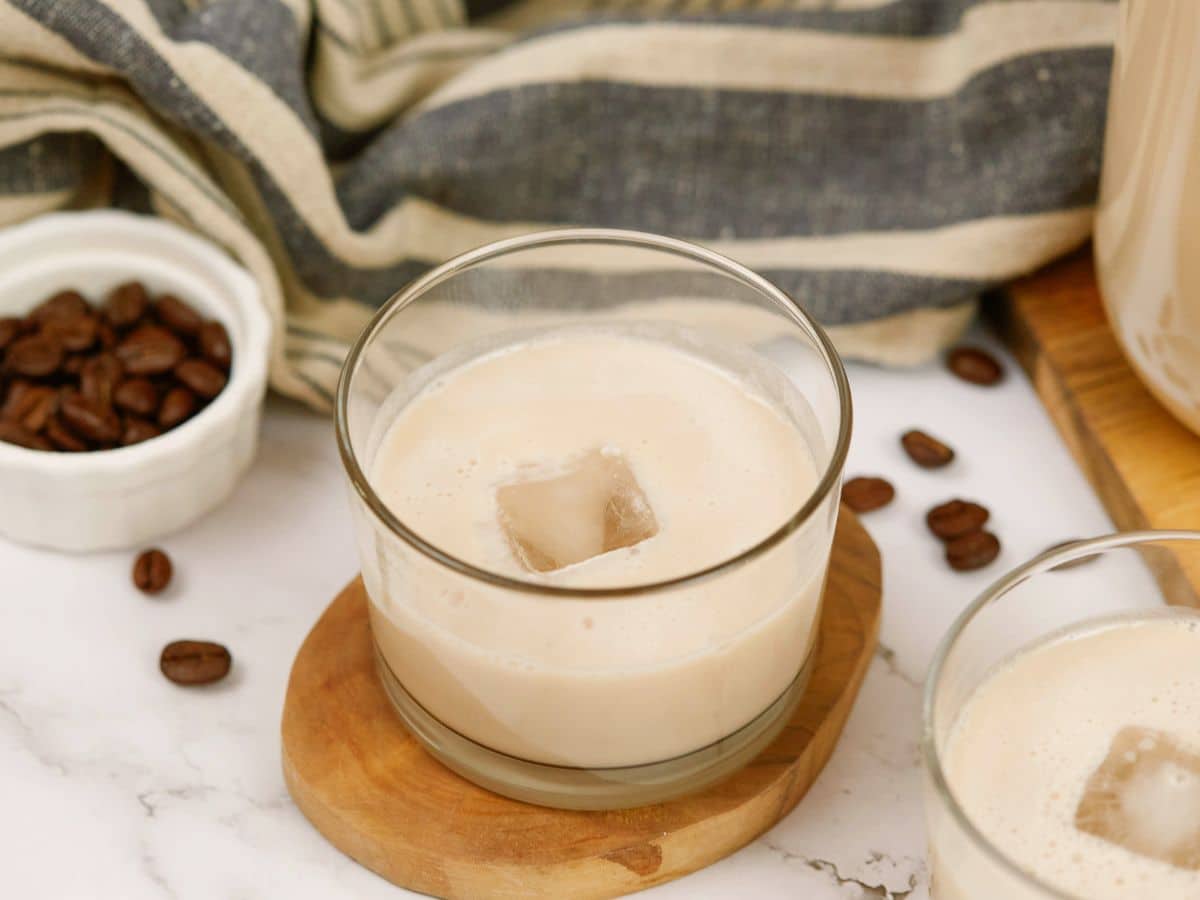 ice cube in center of short glass of vegan Bailey's Irish cream that is on oval wood slice coaster