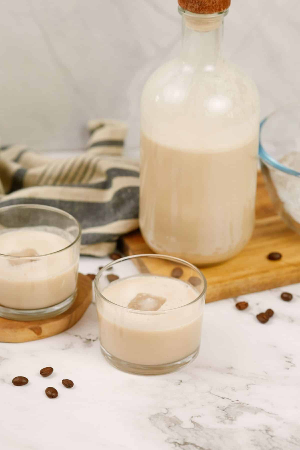 jar of vegan bailey's irish cream on board behind two short glasses of cocktail