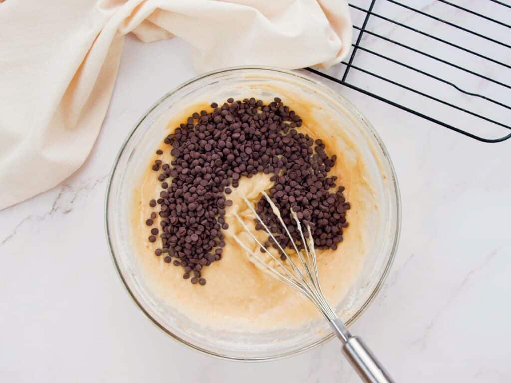 chocolate chips on top of batter in glass bowl with whisk